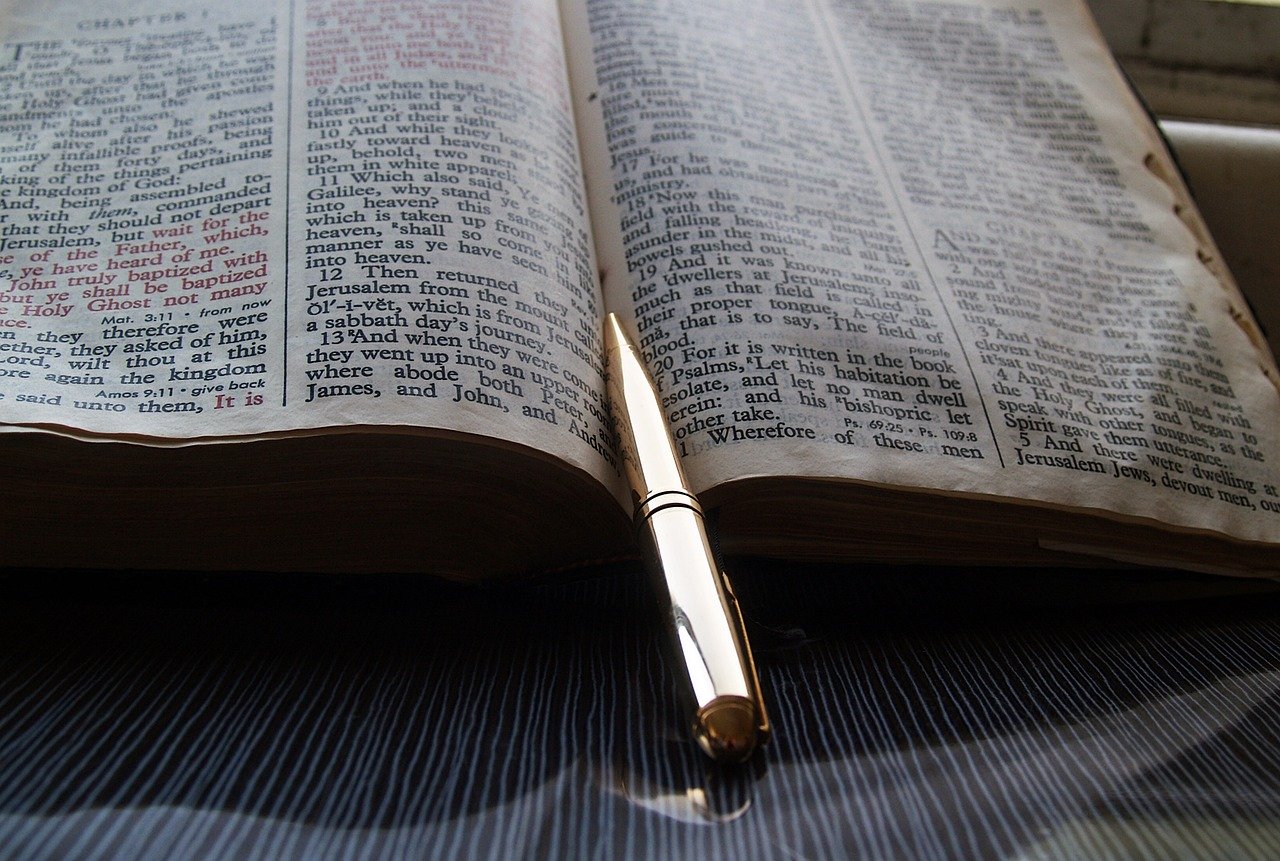 open bible laying flat and angled with shiny gold pen in center crease pointing to the top