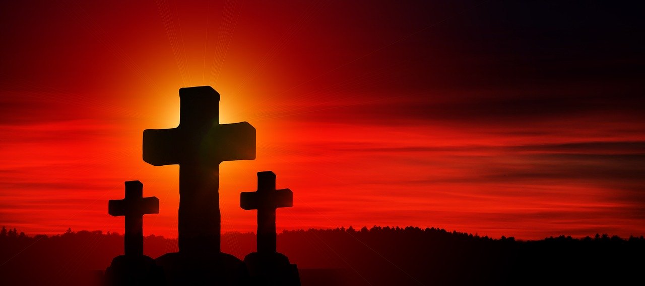 A large stone cross in the middle of two smaller crosses on an elevated hillside with an intense red sky in the background