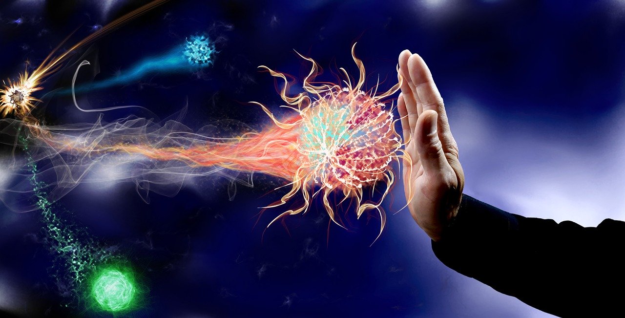 An digitally altered photo of a hand blocking graphical representations of viruses in several different colors as they emerge from a distant point in the upper left corner