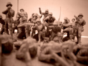 A sepia image of a battalion of toy soldiers standing and kneeling while aiming weapons at another set lying down in the foreground