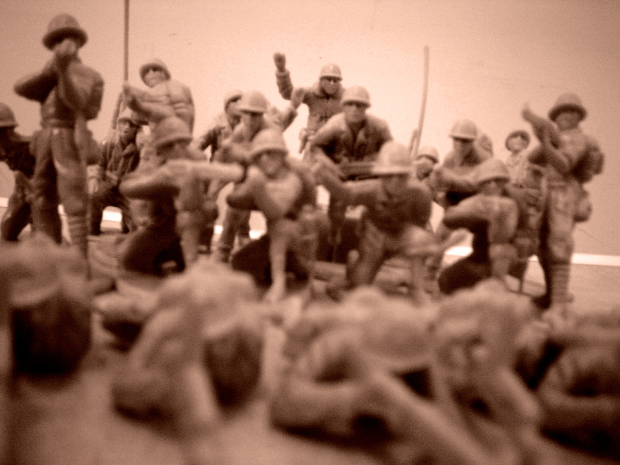 A sepia image of a battalion of toy soldiers standing and kneeling while aiming weapons at another set lying down in the foreground
