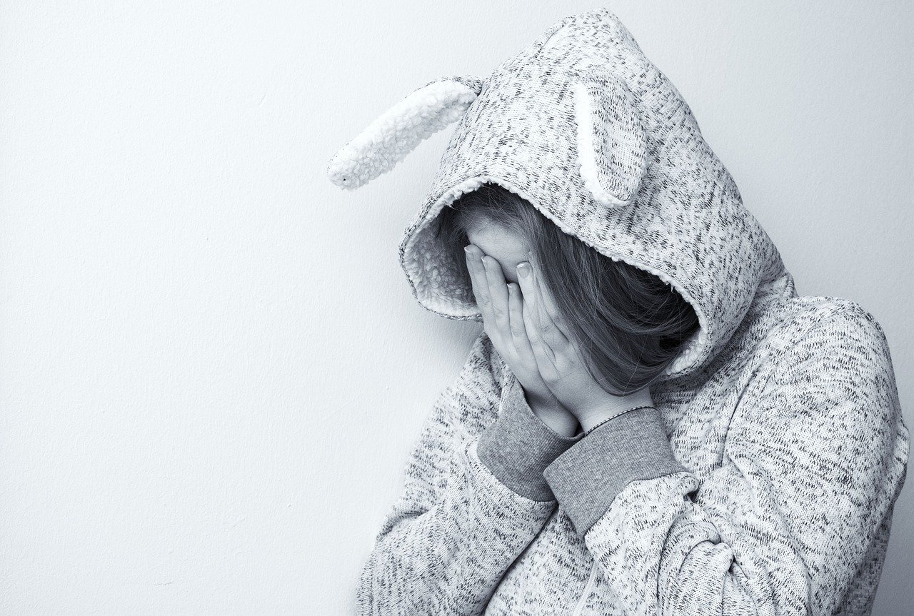 A black and white photo of a girl wearing a hooded sweatshirt with floppy ears and holding her hands over her face a reminder that the Lord will help us irregardless of our age or situation