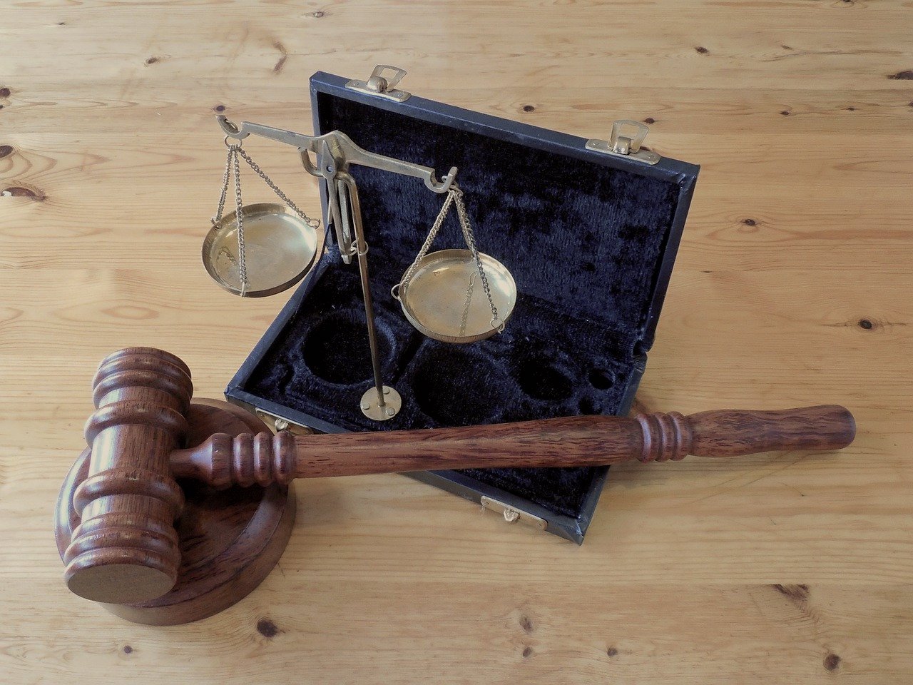 A photo of a wooden gavel and a brass scale of justice set up in its case while resting on a wooden surface.
