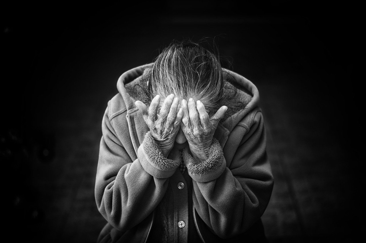 A black and white photo of a solitary older woman wearing a heavy coat with her head leaning down into her hands symbolizing how God hears our cry