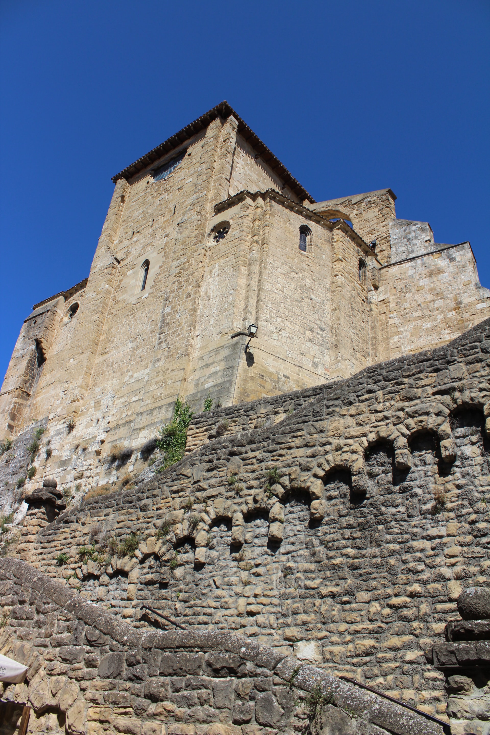 A large old stone building sitting on a high elevation with a decorative stone wall and stairway leading up to it and a deep blue sky in the background