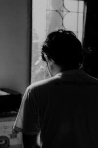 A black and white photo of the rear view of a man with his bowed down in a sun lit room