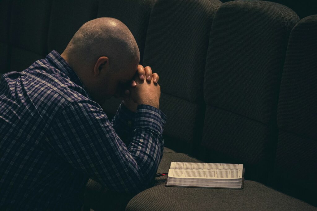 A man kneeling against a row of seats in prayer with a Bible open in front of him symbolizing how to find peace in difficult times