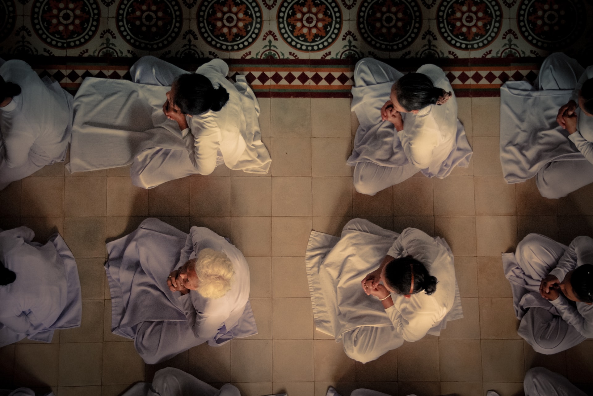 A overhead view of worshippers seated on a tiled floor with folded hands in their lap showing that they have faith but not necessarily faith in God