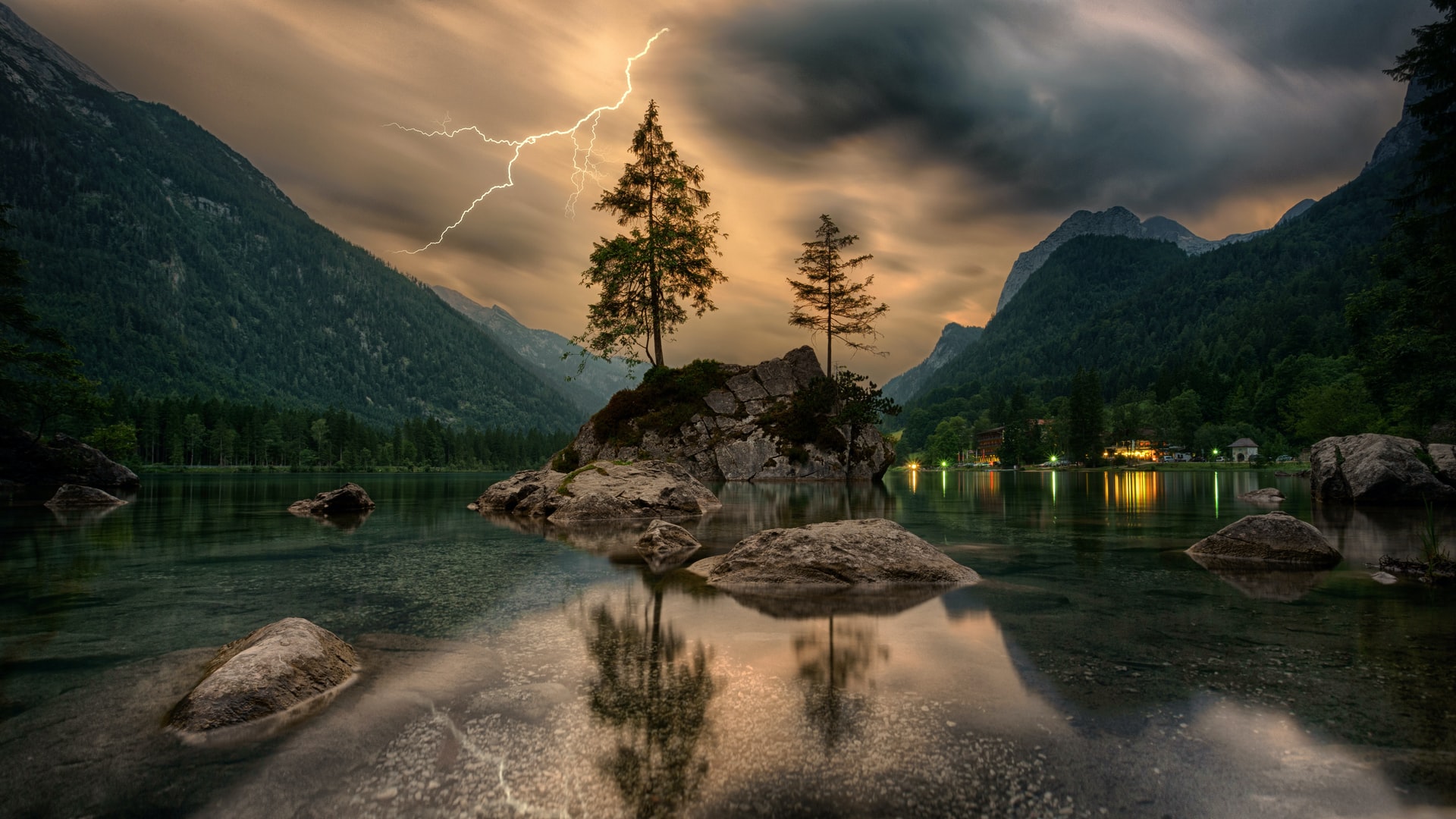 A photo of a calm lake of peace with large mountains, dark clouds, lightning, two tall coniferous trees and an orange sky in the background