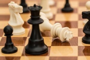Assorted chess pieces on a brown and tan chess board with one piece fallen on its side