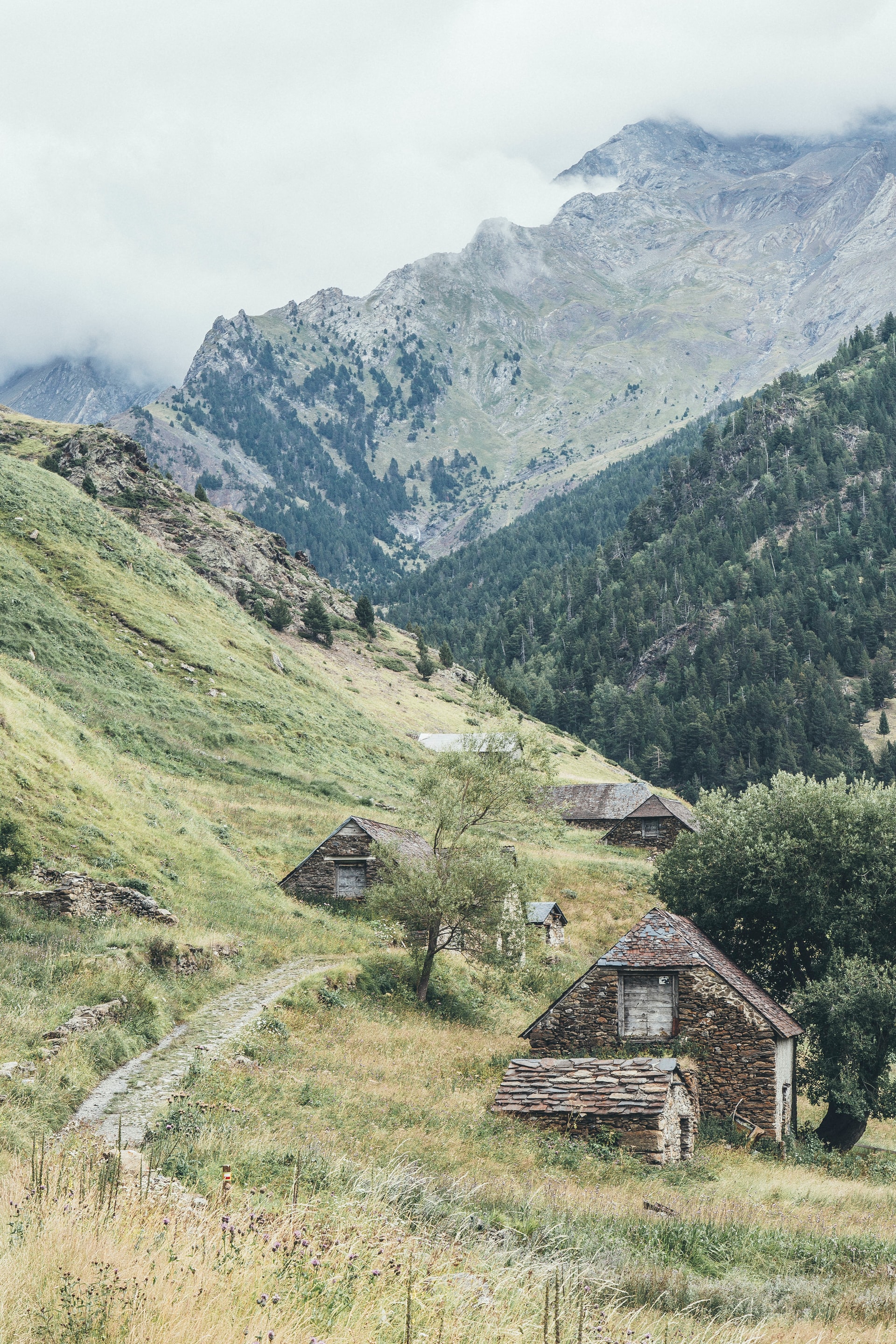Assorted stone cottages on side of a grassy mountain with other mountains and clouds in the background illustrating individuals who may have made the rest stop their destination