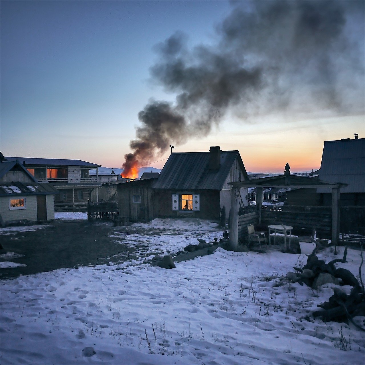 Flames and smoke rising in the distance of small Siberian village with snow on the ground a fading sunset in the background