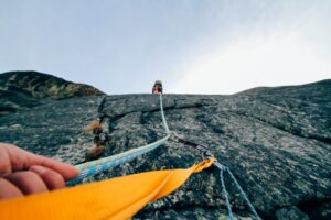 A view from a climber on a sheer mountainside with another climber high up near the top