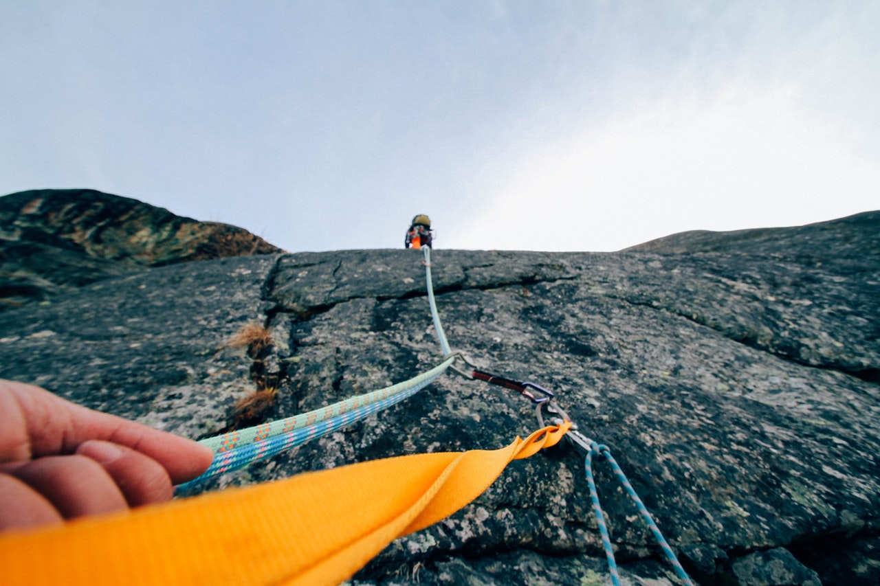A view from a climber on a sheer mountainside with another climber high up near the top