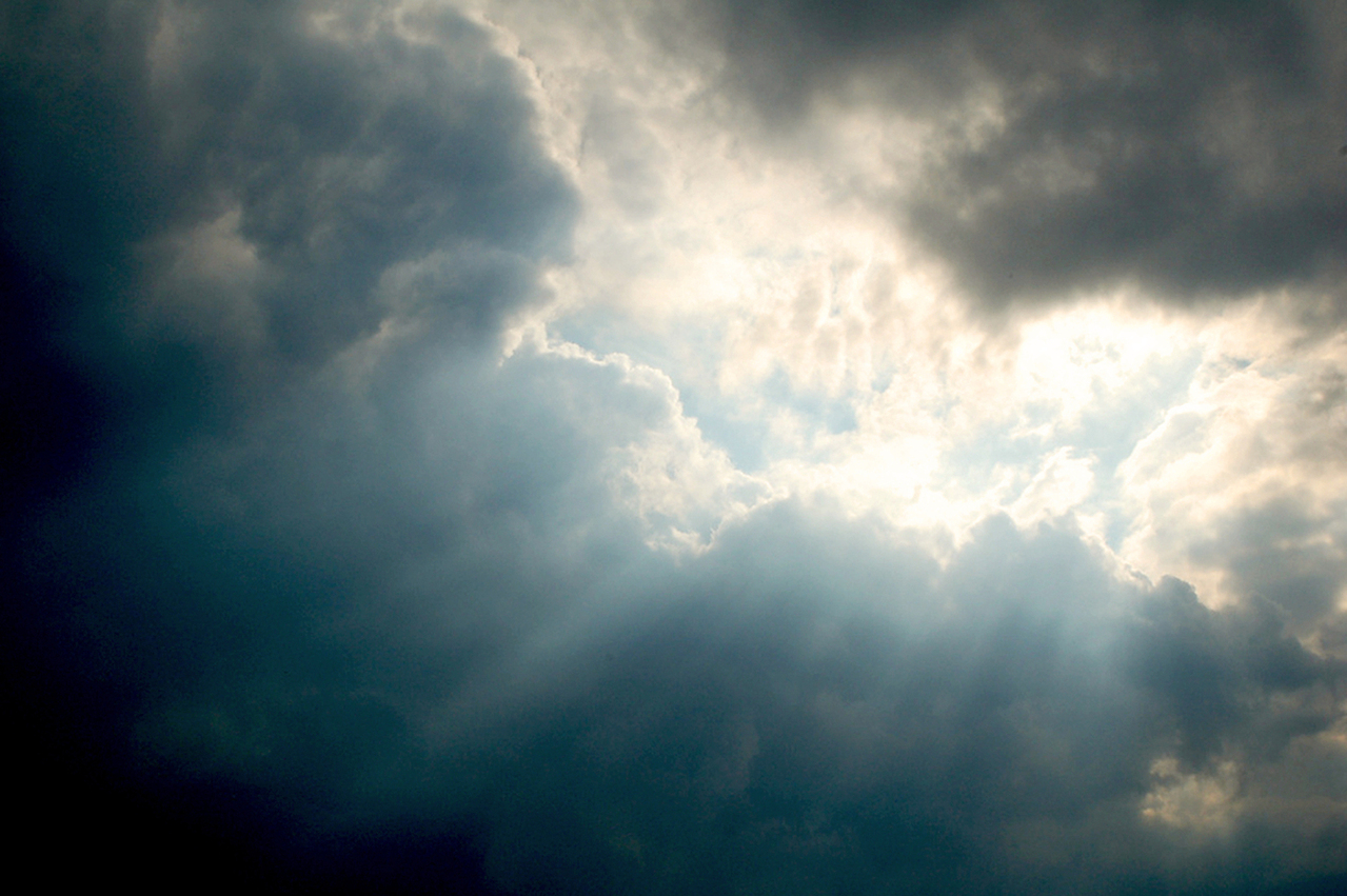 Photo of sun and sun beams through a cluster of blue and grey clouds