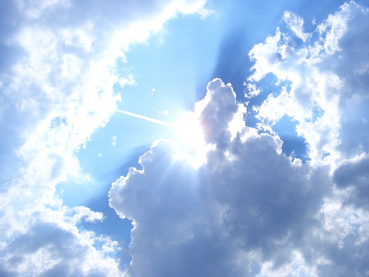 Sun poring through assorted clouds with a light blue sky in the background