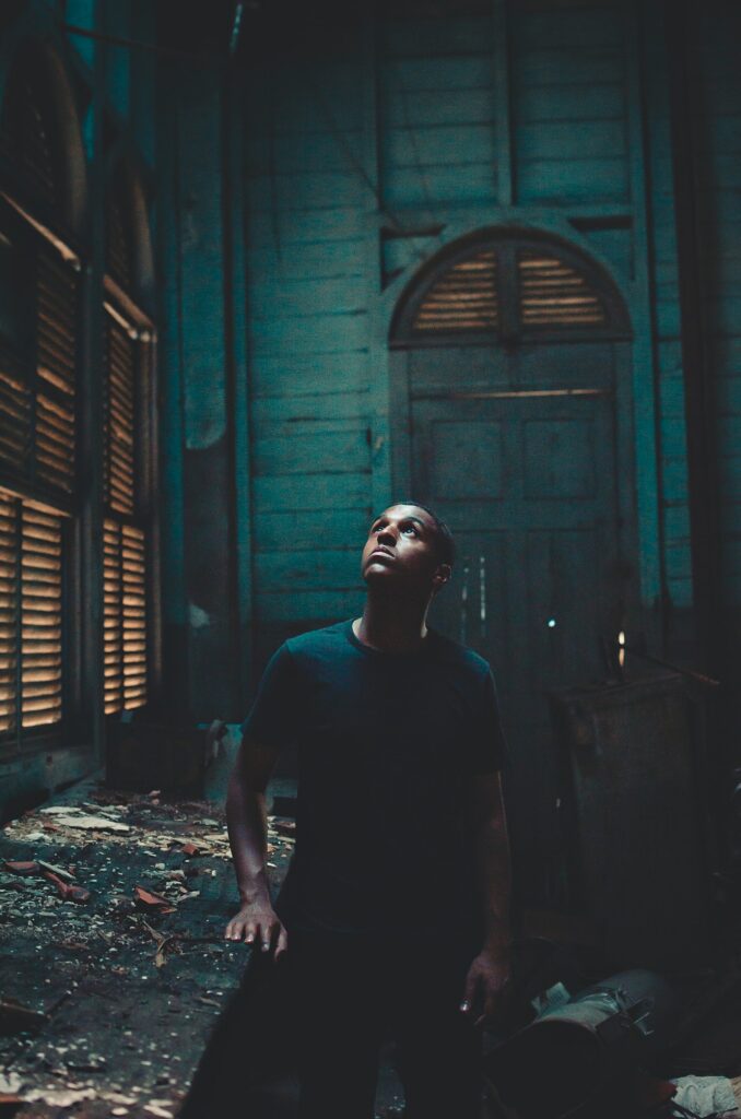An young African-American man looking upward with light shining on his face in a dilapidated old green hued room