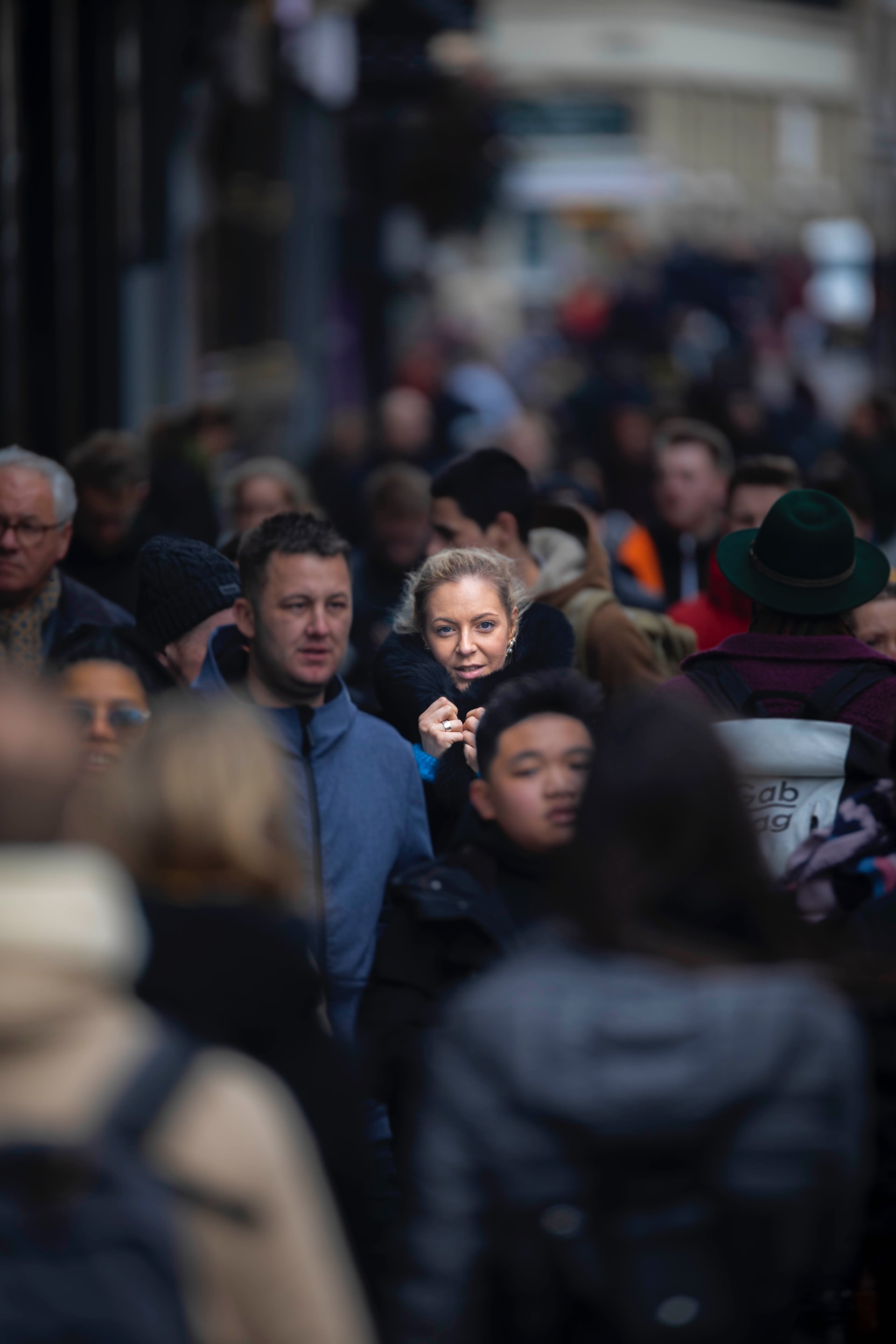 A photograph of a Caucasian woman, highlighted with sunlight, walking in a crowded street of mixed people