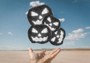 Image compilation of a collection of four assorted small black and white jack-o-lanterns representing fear suspended above an outstretched hand in the middle of an open sandy plain with blue sky and clouds in the background