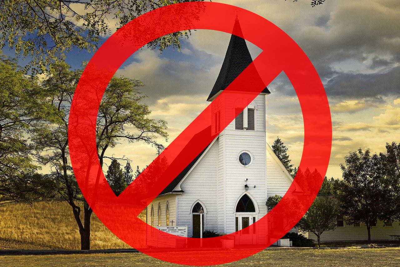 A white country chapel with a large tree on the left with mixed clouds in the sky above and a large red circle with slash through it superimposed on the chapel