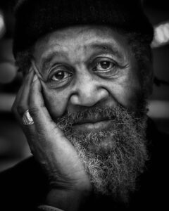 A black and white head shot of an older African-American man with his head leaning against his raised right hand and a look of depression or despair on his face
