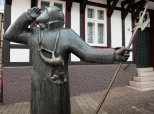 A photo of a medieval watchman statue with a tudor style building in the nearby background