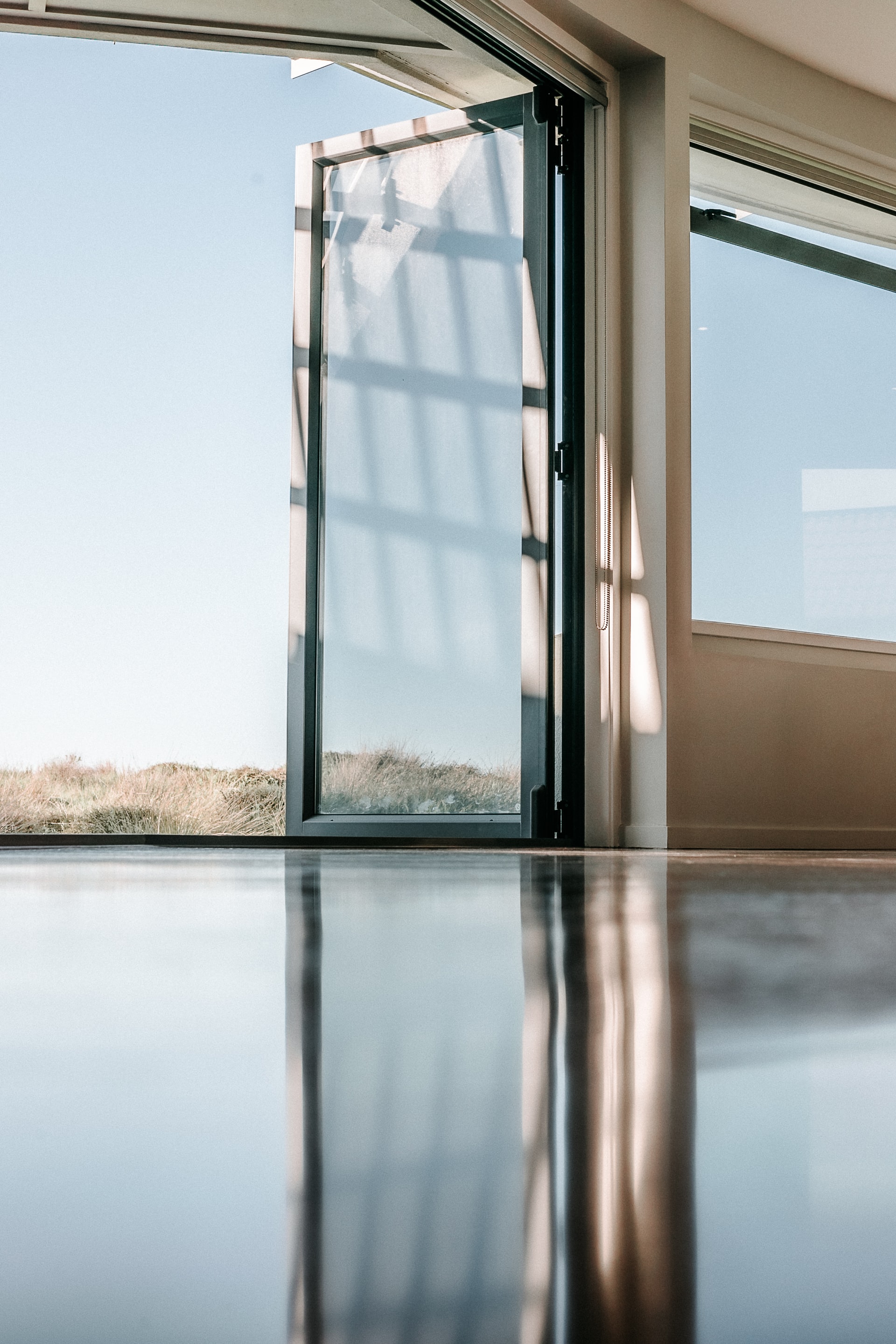 A ground level photo of a glass door opened to the outdoors and reflecting on the glossy floor