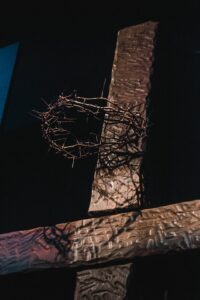 Closeup photo of the upper portion of a wooden cross on a black background with a crown of thorns attached near the top