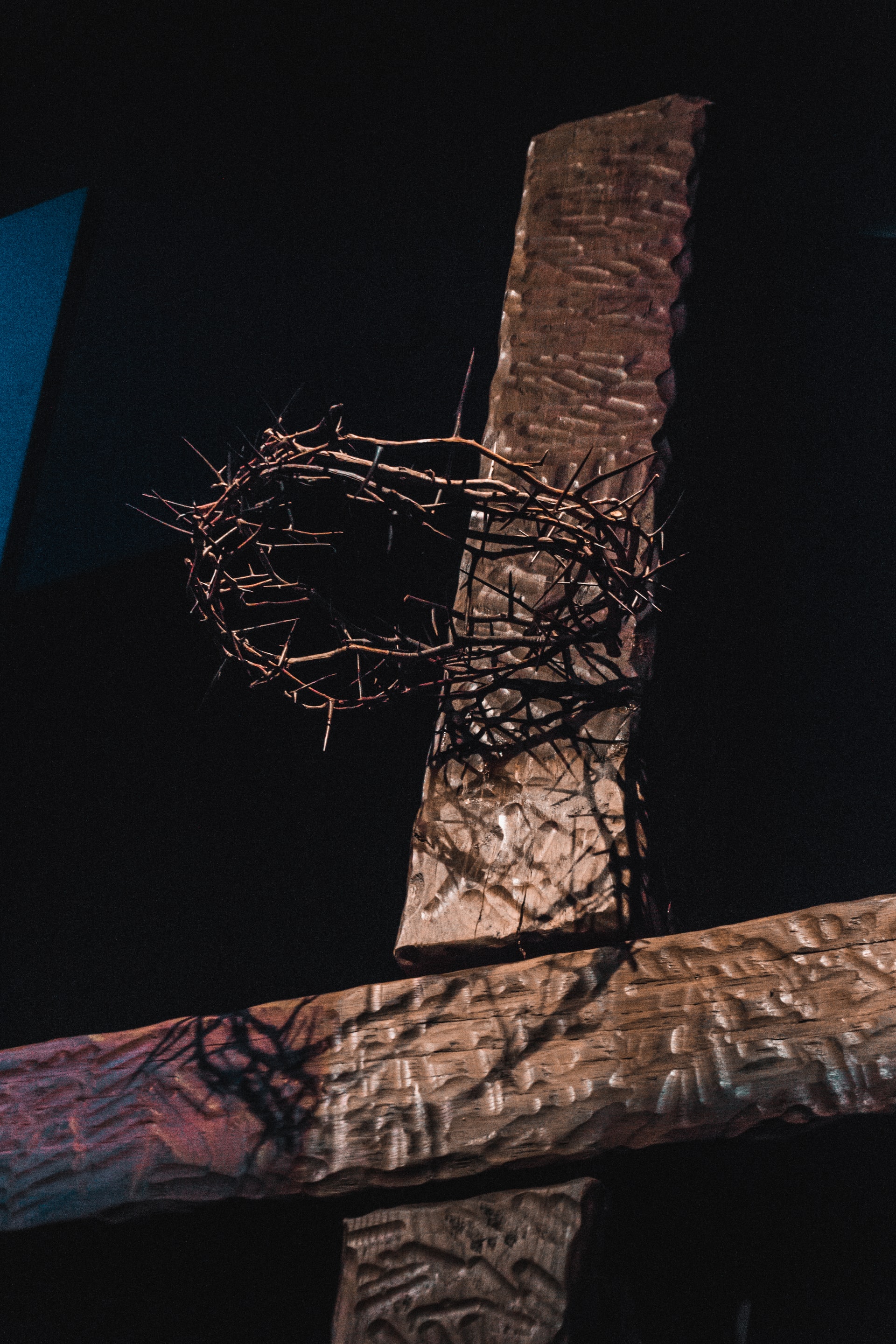 Closeup photo of the upper portion of a wooden cross on a black background with a crown of thorns attached near the top