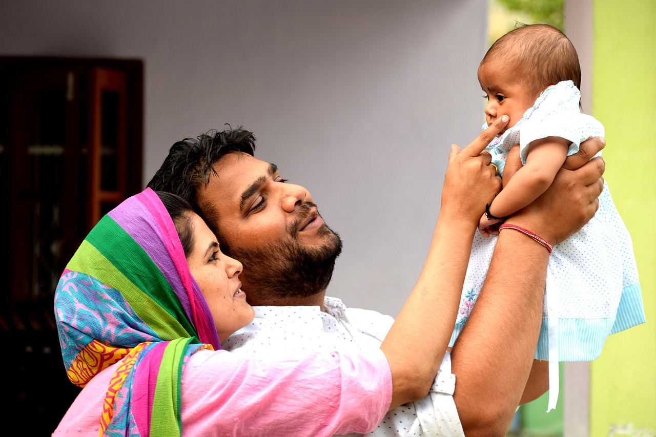 A young Indian couple holding a child in the air and smiling