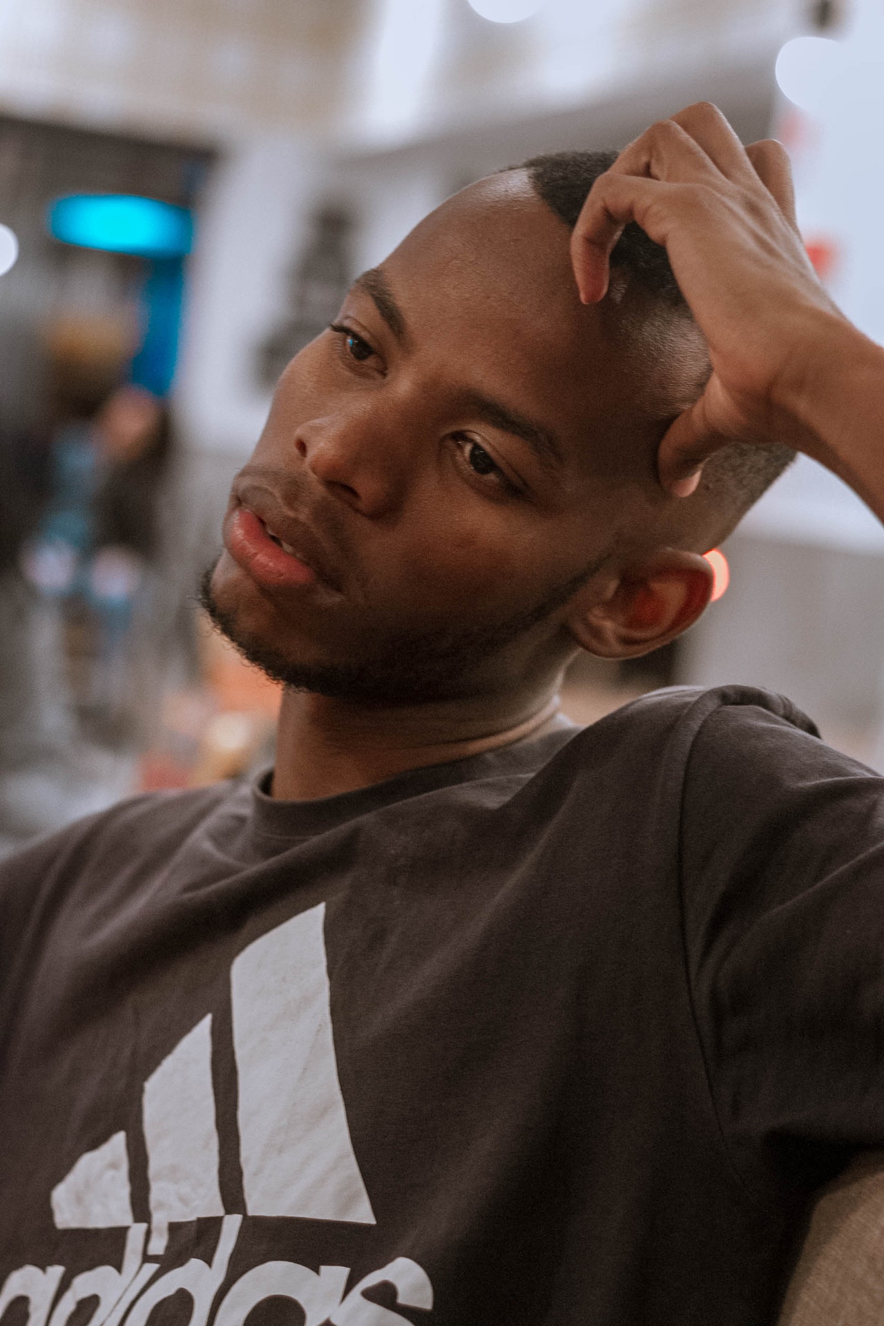 A photographic portrait of a young African-American man wearing a black Adidas branded t-shirt with his left arm supporting his angle leaning head and an expression of distant thought on his face