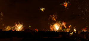 A handful of very distant fireworks over a city skyline on a dark night