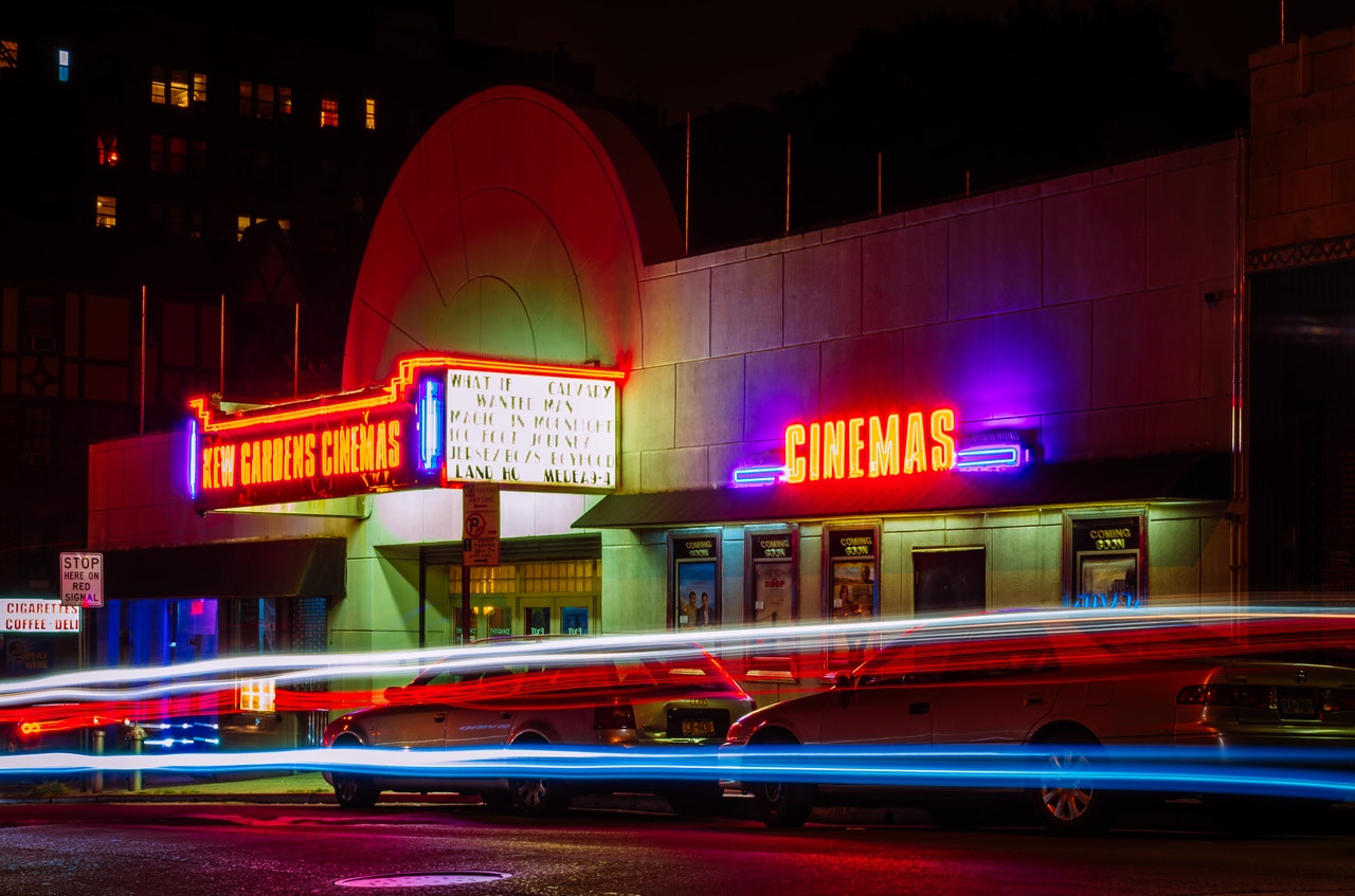 Night view of a movie theater exterior with neon lights displaying the theater's name and streaks of light from passing vehicle tail and headlights