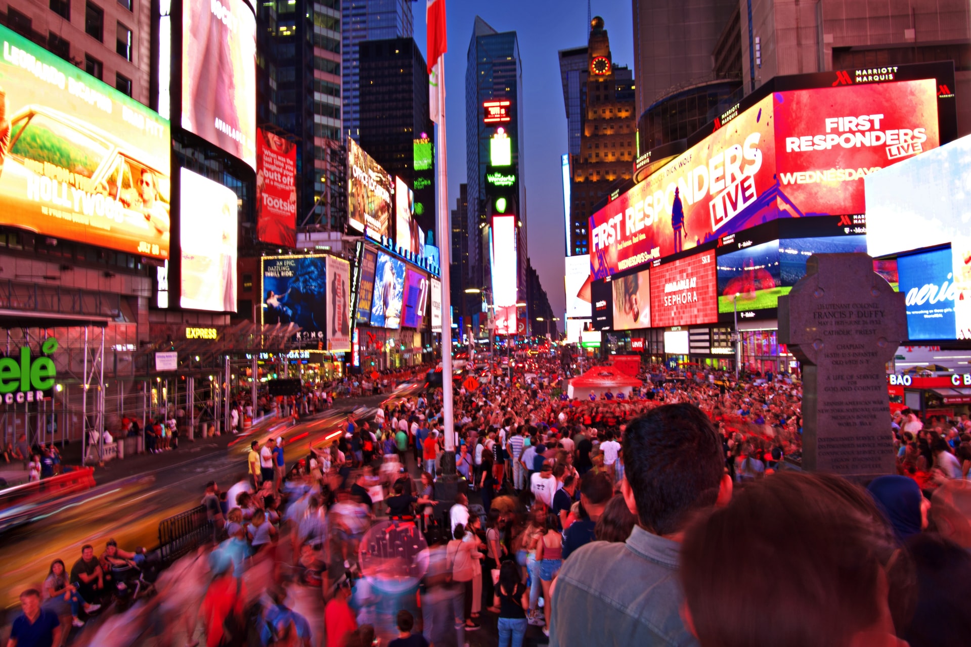 A photo looking down Times Square in New York City at night with hundreds of people and brightly lit full colored electronic billboards on the buildings of both sides of the street
