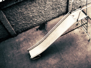 An overhead black and white photo of a playground slide near a textured concrete wall