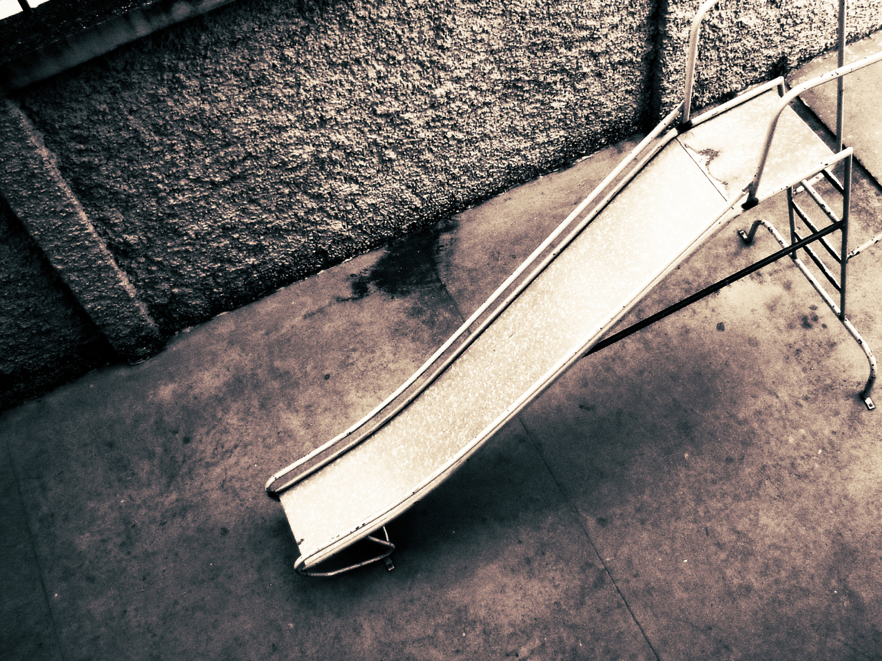 An overhead black and white photo of a playground slide near a textured concrete wall