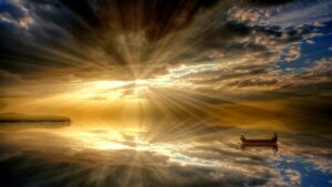 A bright clouded sky filled with the beams of a late afternoon sun reflecting on a very large, still body of water with a small boat near the lower right of the picture