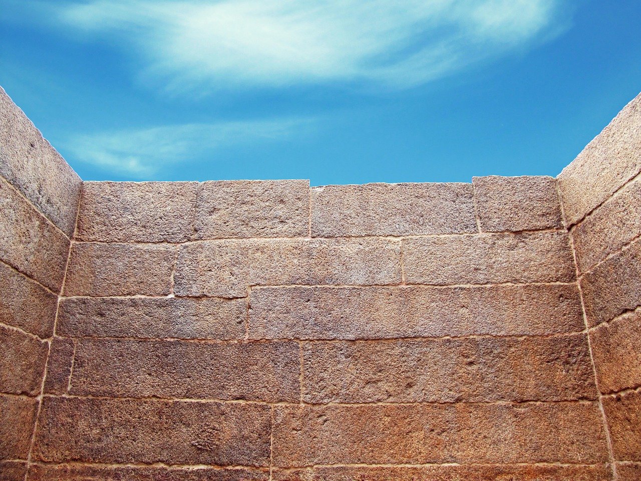 Interior of a tall, light brown concrete block wall structure with blue sky and clouds above