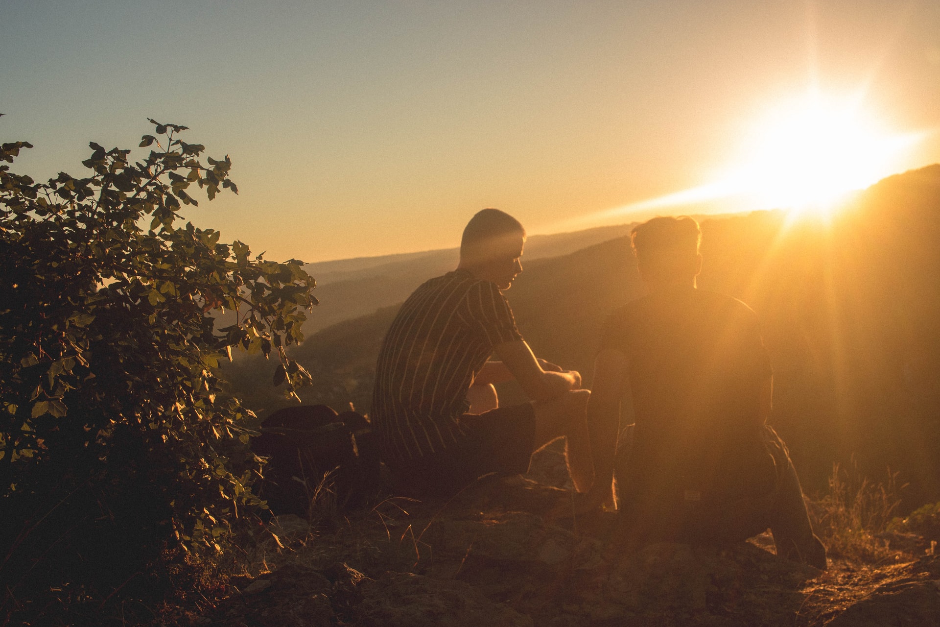 Two young men sitting and talking in fellowship on a sunlit hillside with the sun rising in the background