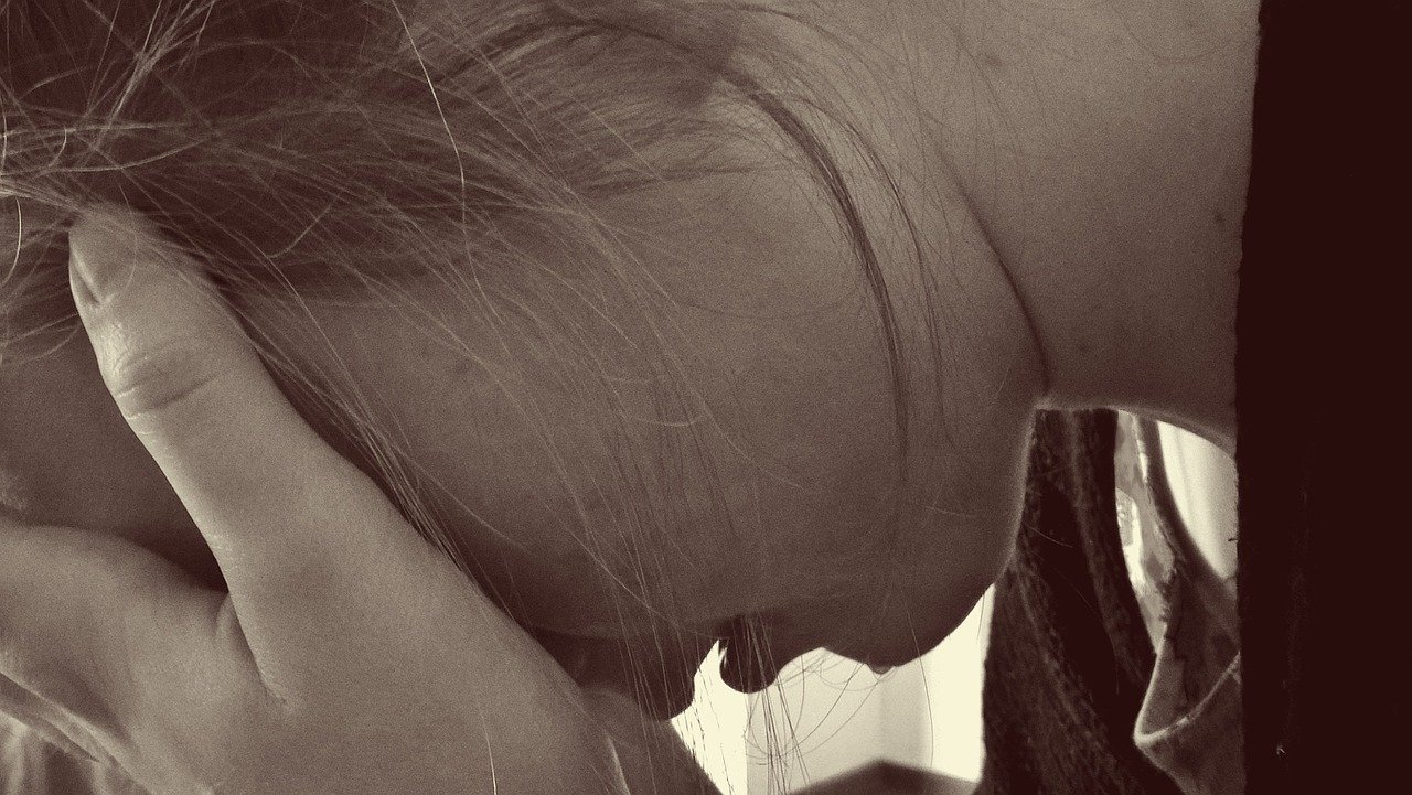 Closeup sepia style photo of young woman with head in hands and crying