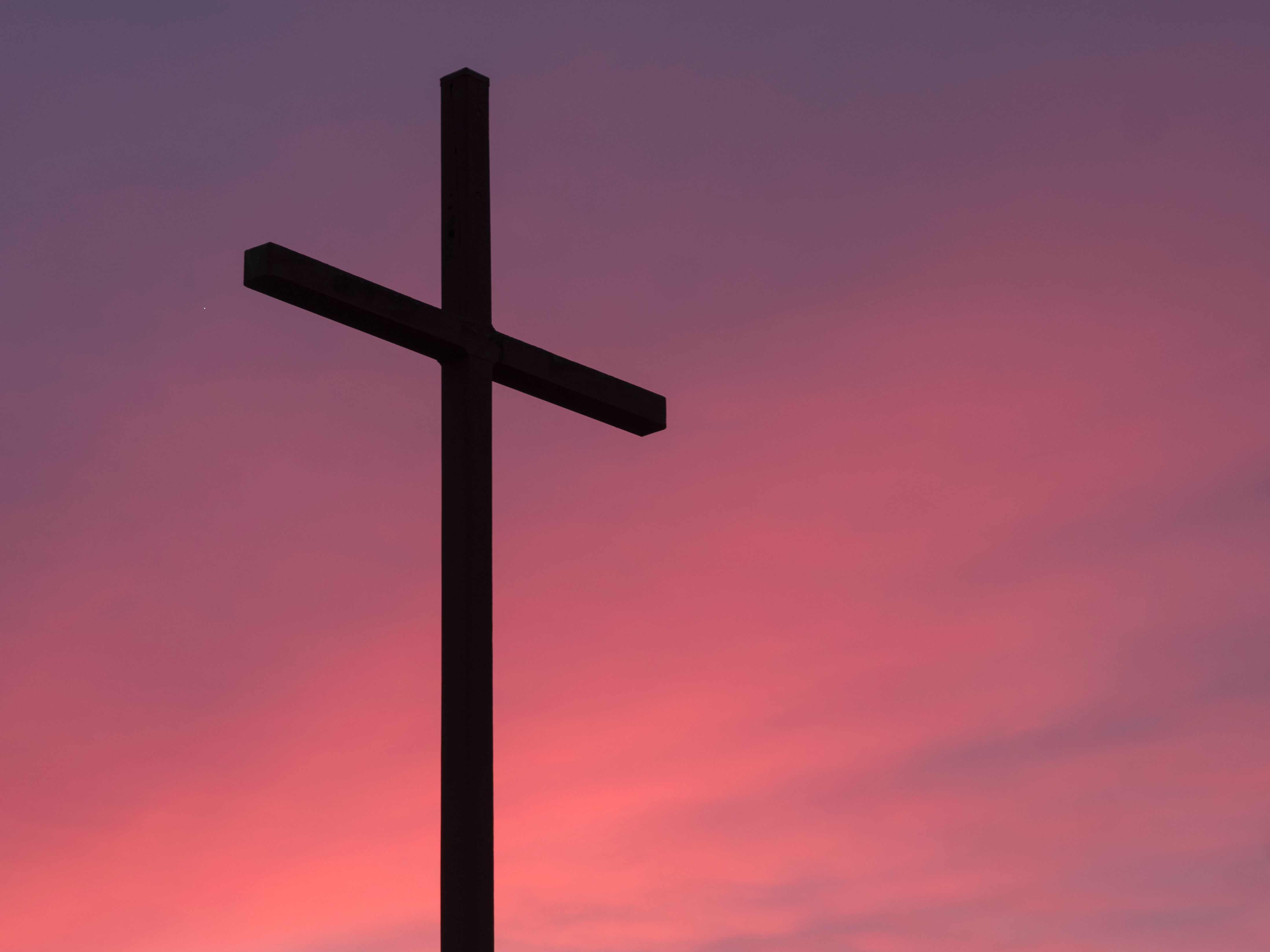 A silhouette of a large cross at an angle with a pink clouded sky in the background