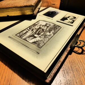 A open page of an old photo album laying flat with another book on an old wood desk with a bright light overhead
