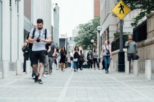 An assorted collection of people walking on a street between two large buildings on a hazy afternoon