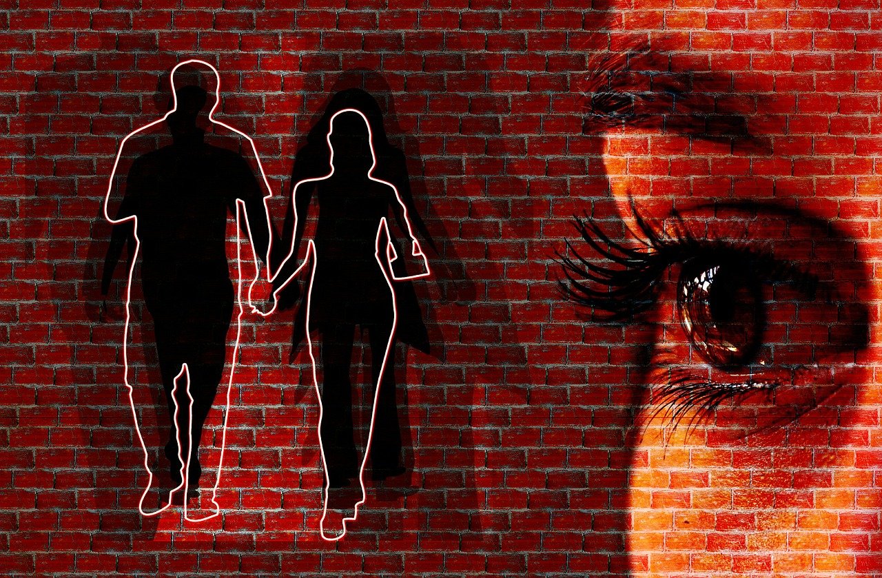 A graphical image illustrating self-centered human jealously as opposed to our flirtation to false gods of godly jealousy through the display of a brick wall with white outlines of a silhouette of a male and female walking together while holding hands and a superimposed image of a part of a woman's face with the eye and eyebrow portion displayed prominently.