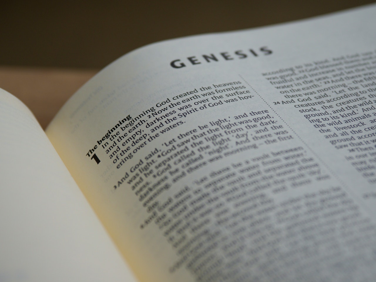 A Bible opened to the first chapter of the book of Genesis with lower portions of it out of focus