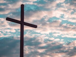 A photo of a silhouette of a cross against slightly pink tinted clouds and blue sky