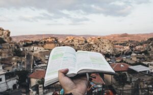 A single hand holding up a open book with underlining onto a Mediterranean type city and countryside