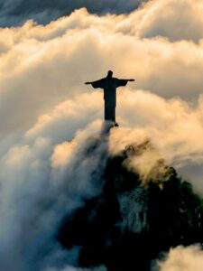 A photo of a statue of Jesus high on a mountain top surrounded in clouds and sunlight