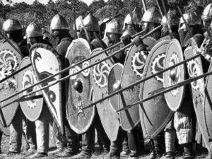 A black and white photo of a group of Medieval solders in full battle gear including swords, spears, and shields containing various crests