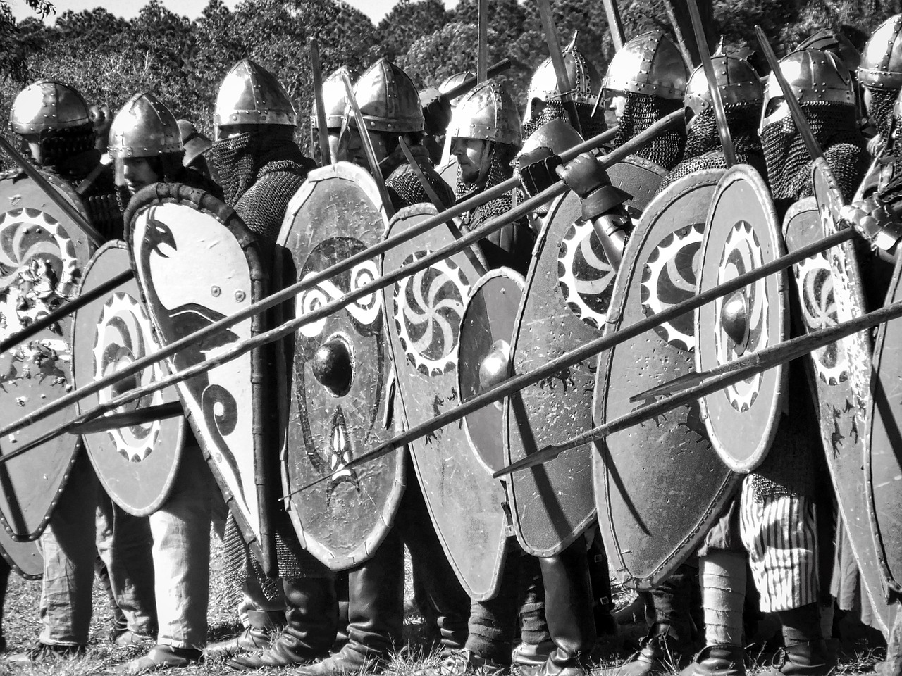 A black and white photo of a group of Medieval solders in full battle gear including swords, spears, and shields containing various crests